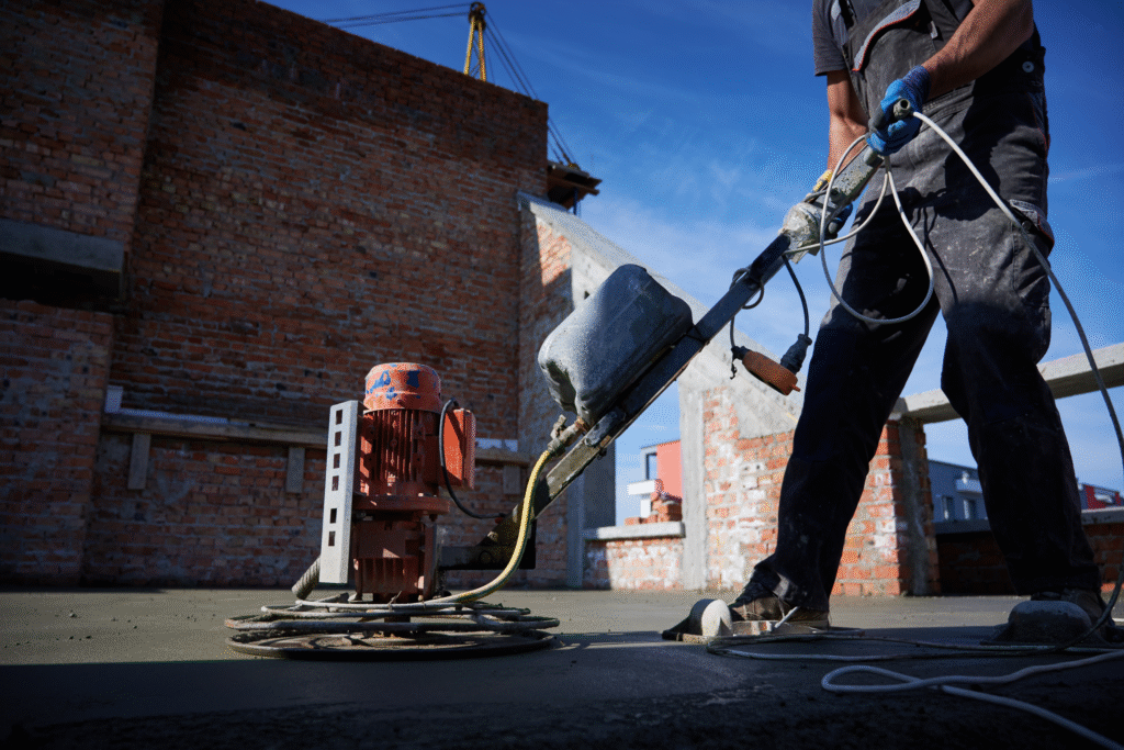 Construction worker using a power trowel to smooth and finish freshly poured concrete on a rooftop or large slab.