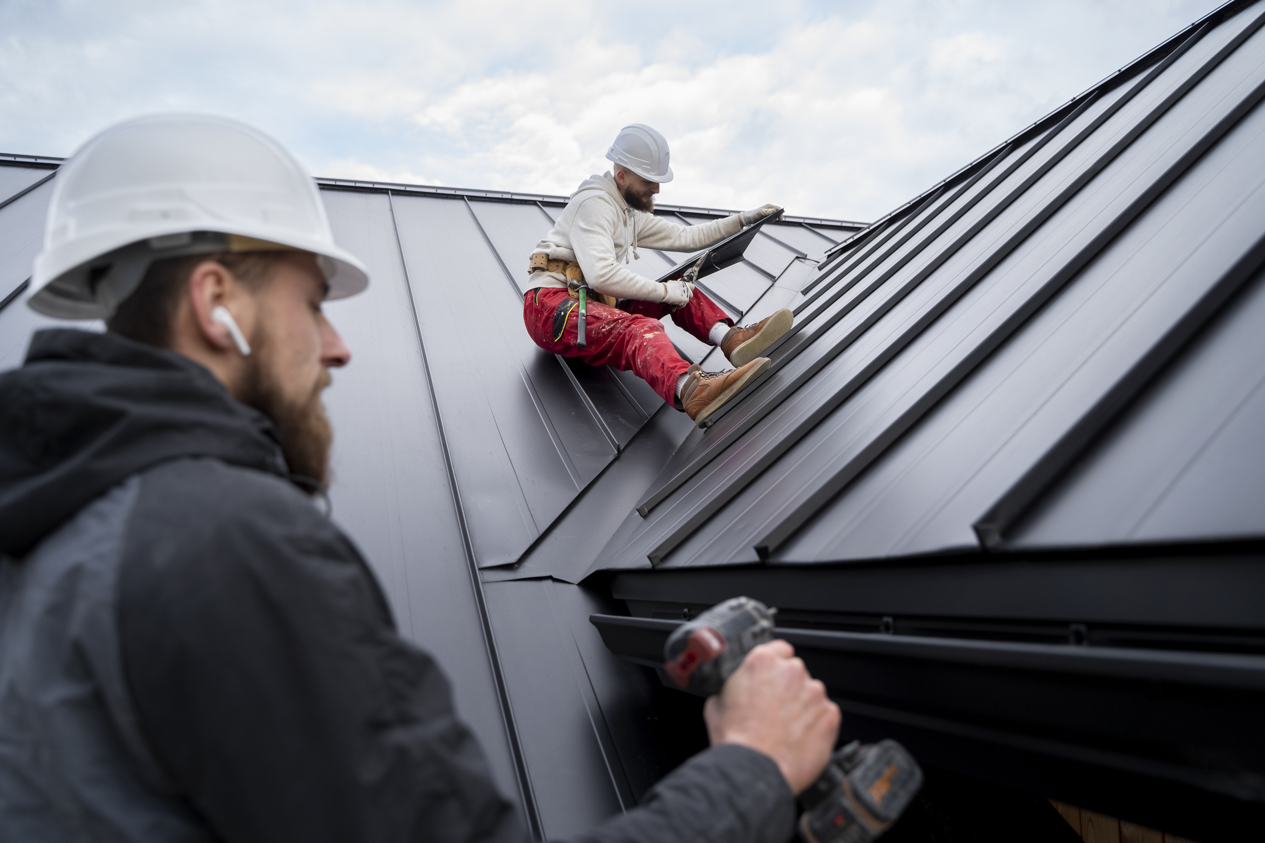 Two professional roof cleaning or maintenance technicians working on a steep, black metal roof, emphasizing safety and skill for warranty-safe cleaning.